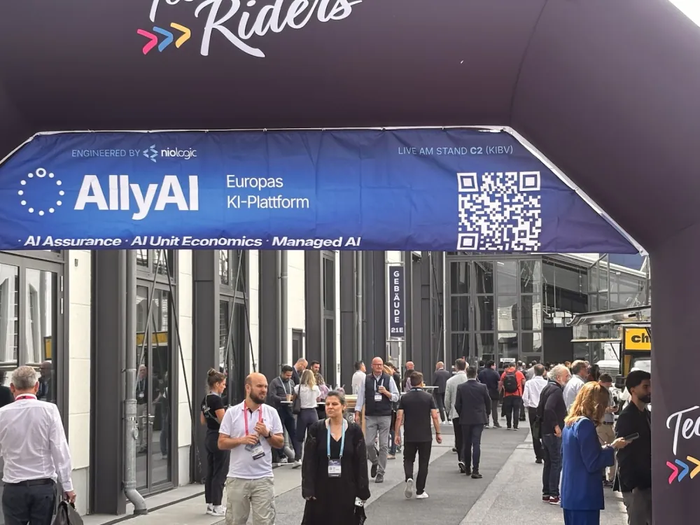 AllyAI-Banner am Eingangsbogen des niologic-Messeauftritts, Besucher auf dem Veranstaltungsgelände